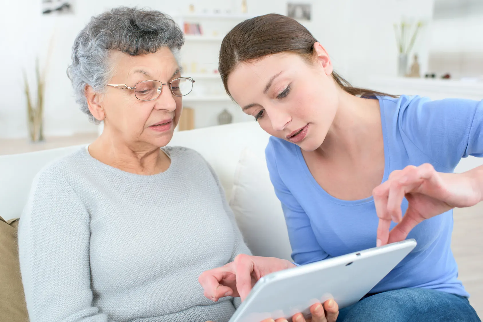 Junge Frau erklärt einer Seniorin etwas auf dem Tablet